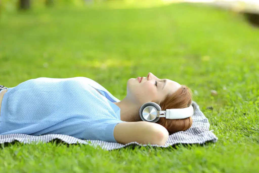 Woman wearing headphones lying back on the grass