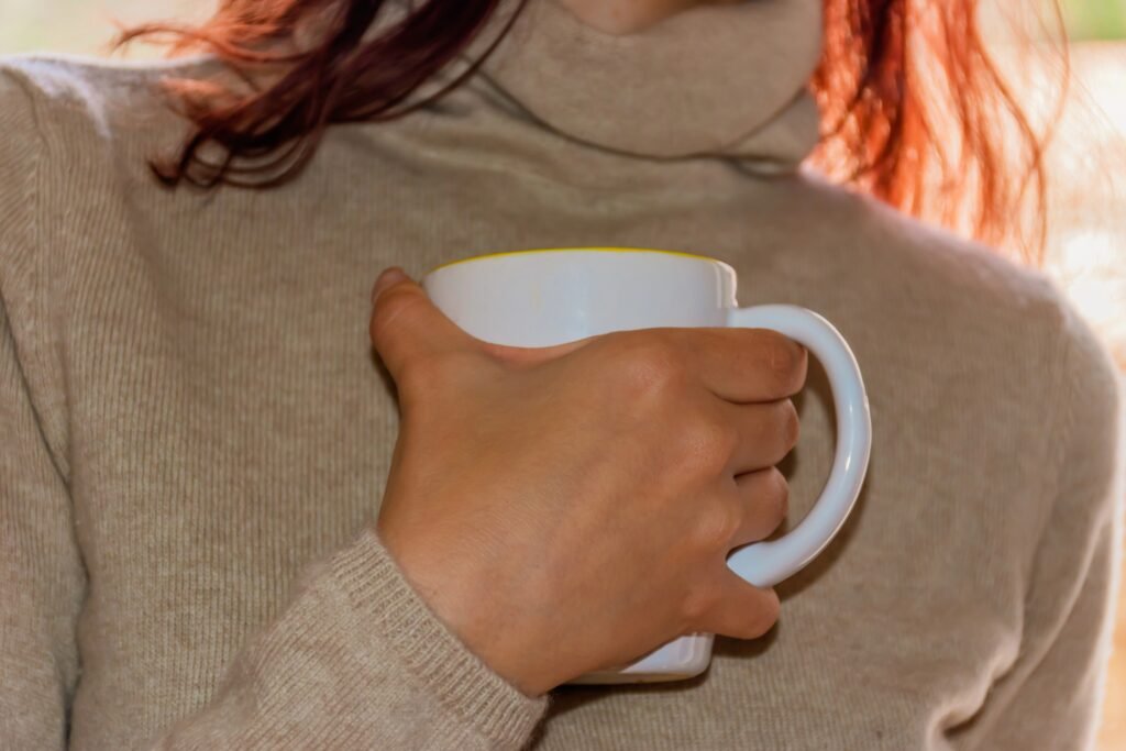 Close up woman's hand holding coffee mug to chest
